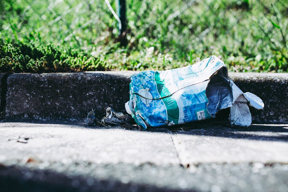 A crumpled plastic bag with a blue and white print is discarded on a concrete curb, partially folded with some torn edges and creases visible. The bag appears to contain or have contained paper or oth